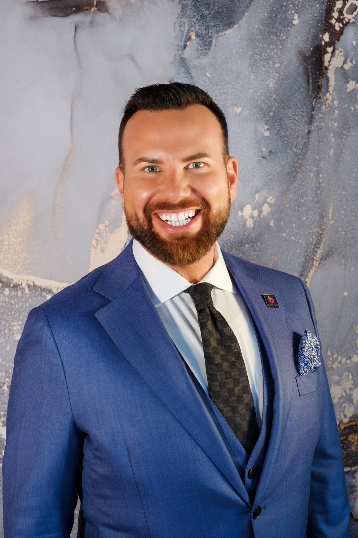 Portrait of Justin in a blue suit and patterned tie, smiling.
